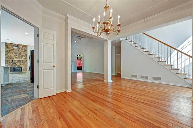 unfurnished living room with vaulted ceiling, ceiling fan with notable chandelier, a stone fireplace, light hardwood / wood-style floors, and crown molding