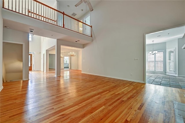 unfurnished living room with a towering ceiling, ceiling fan with notable chandelier, and light hardwood / wood-style flooring