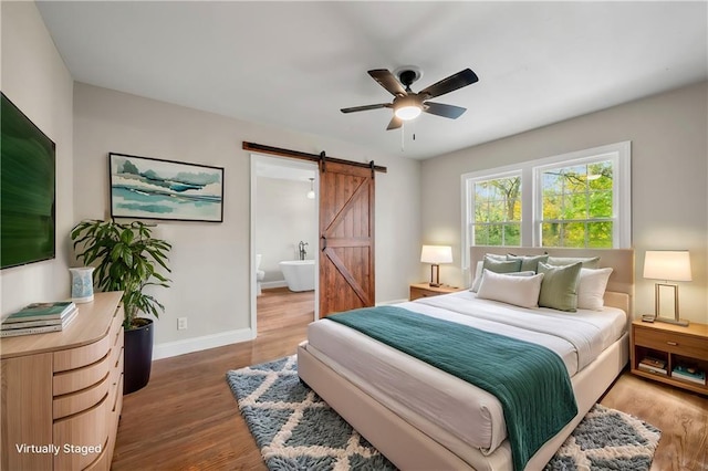 bedroom featuring hardwood / wood-style flooring, ceiling fan, a barn door, and ensuite bath