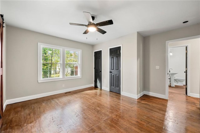 unfurnished bedroom with ceiling fan, wood-type flooring, and connected bathroom