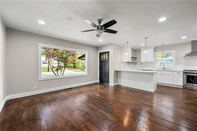 kitchen featuring sink, stainless steel stove, white cabinets, decorative backsplash, and wall chimney exhaust hood