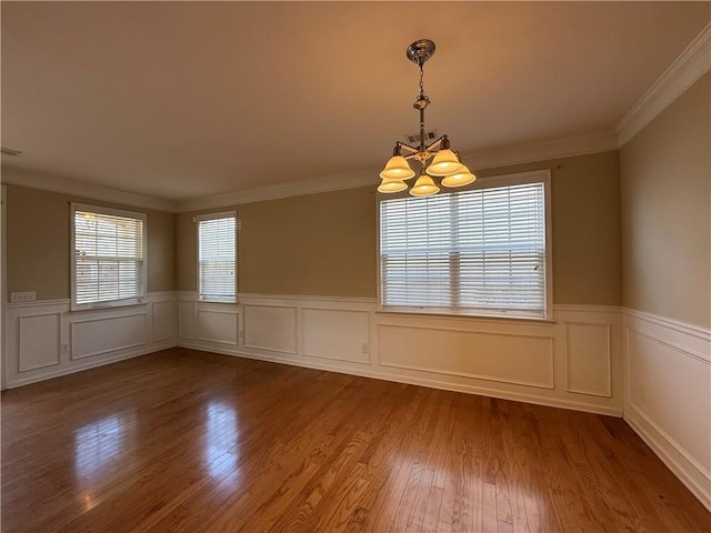 empty room with a notable chandelier, ornamental molding, a wainscoted wall, and wood finished floors