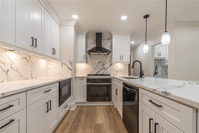 kitchen featuring decorative light fixtures, sink, white cabinets, wall chimney range hood, and black appliances