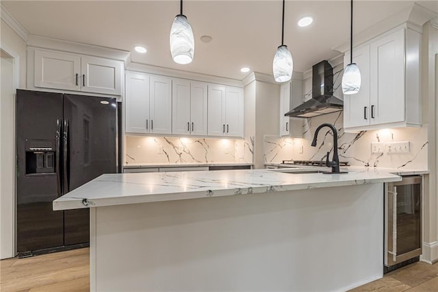 kitchen featuring hanging light fixtures, wall chimney exhaust hood, white cabinetry, black refrigerator with ice dispenser, and beverage cooler