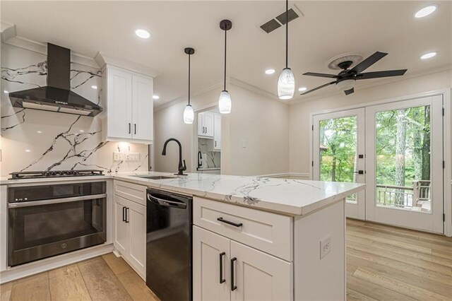 kitchen featuring appliances with stainless steel finishes, wall chimney exhaust hood, white cabinetry, backsplash, and ceiling fan