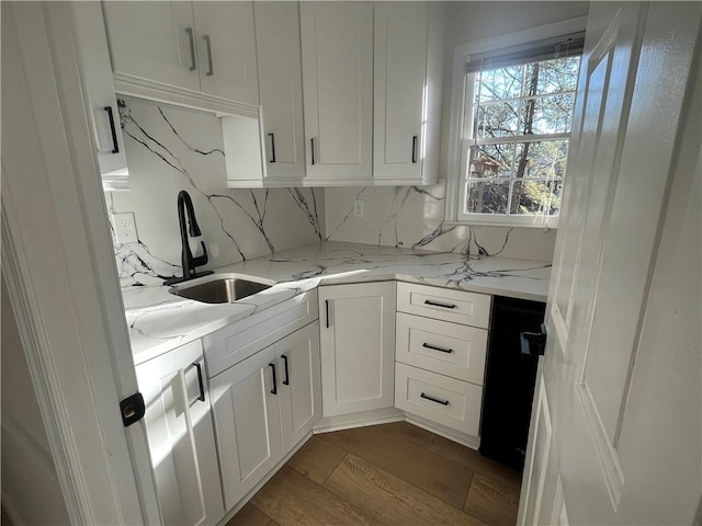 kitchen with white cabinetry, sink, backsplash, light stone counters, and light hardwood / wood-style flooring