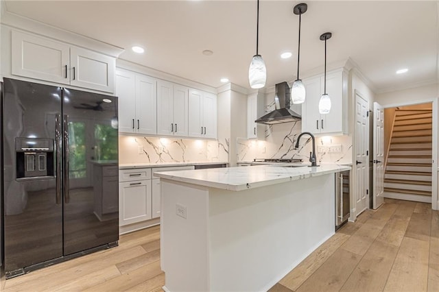 kitchen with tasteful backsplash, white cabinetry, hanging light fixtures, wall chimney range hood, and black fridge with ice dispenser