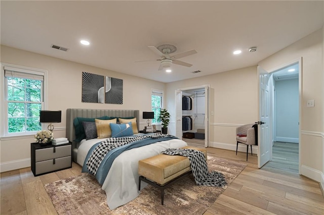 bedroom with a walk in closet, ceiling fan, light hardwood / wood-style floors, and a closet