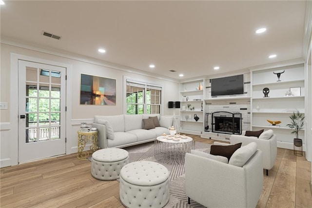 living room featuring ornamental molding, built in shelves, light hardwood / wood-style flooring, and a tile fireplace