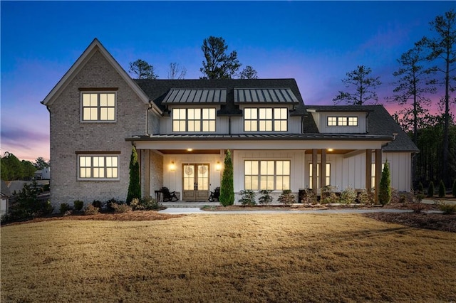 back house at dusk with covered porch, a yard, and french doors