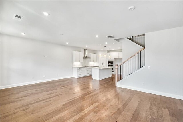 unfurnished living room featuring stairs, baseboards, a sink, visible vents, and light wood-style flooring