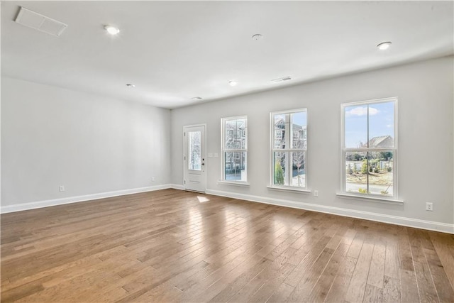 unfurnished room with wood-type flooring, baseboards, and visible vents