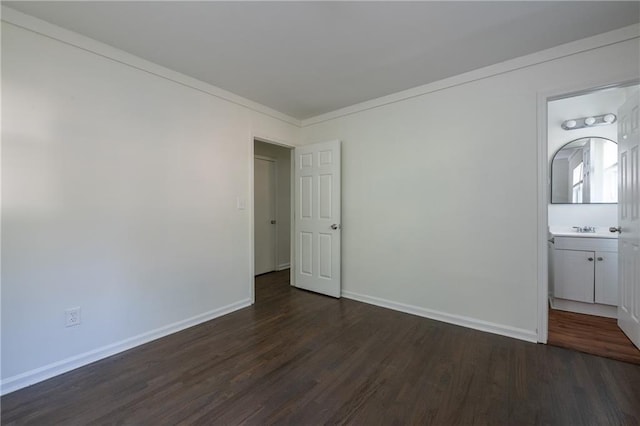 unfurnished bedroom featuring crown molding, dark wood-type flooring, sink, and ensuite bathroom