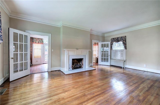 unfurnished living room featuring a premium fireplace, hardwood / wood-style floors, radiator heating unit, ornamental molding, and french doors