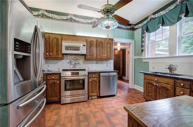 kitchen with sink, appliances with stainless steel finishes, dark tile patterned floors, ceiling fan, and decorative backsplash