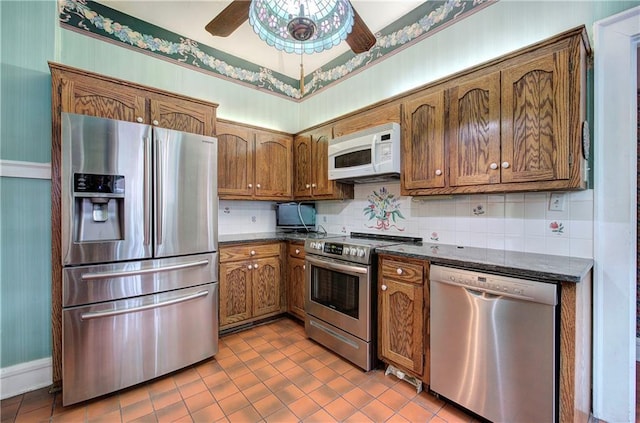 kitchen featuring tasteful backsplash, dark stone countertops, tile patterned flooring, ceiling fan, and stainless steel appliances