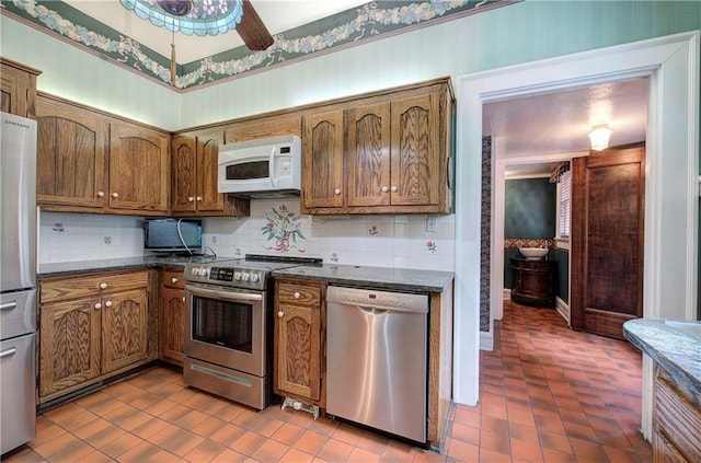 kitchen featuring dark stone countertops, decorative backsplash, ceiling fan, and appliances with stainless steel finishes