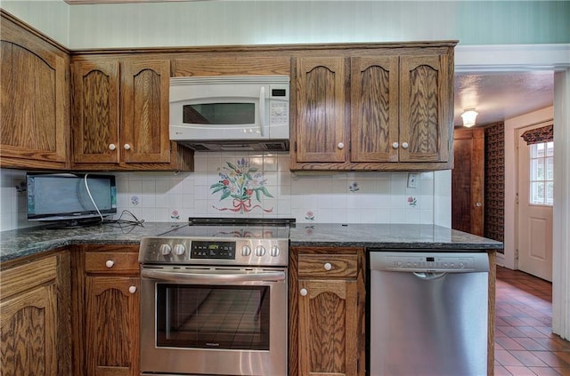 kitchen featuring tasteful backsplash, appliances with stainless steel finishes, and dark stone countertops