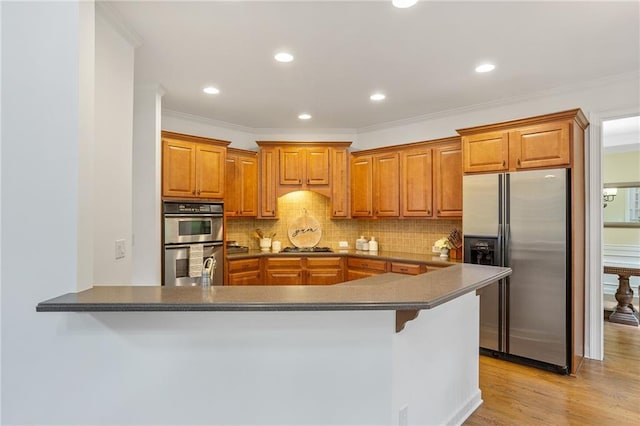 5355 Highland Pine Ln, Mableton, GA 30126 - kitchen featuring appliances with stainless steel finishes, brown cabinetry, decorative backsplash, a peninsula, and light wood finished floors