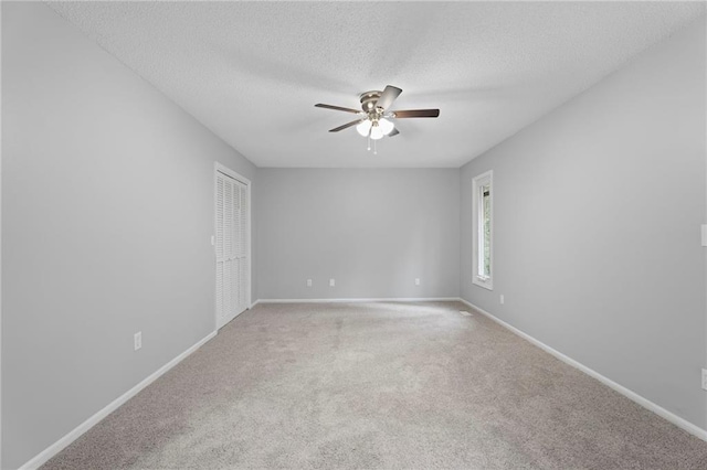 spare room with a textured ceiling, baseboards, a ceiling fan, and light colored carpet