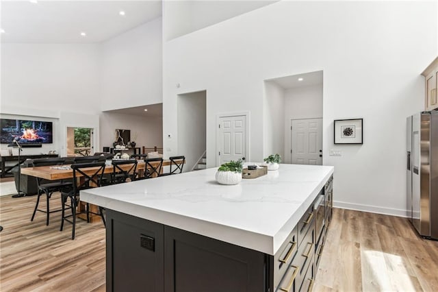 kitchen with stainless steel fridge, open floor plan, dark cabinets, a center island, and light stone countertops