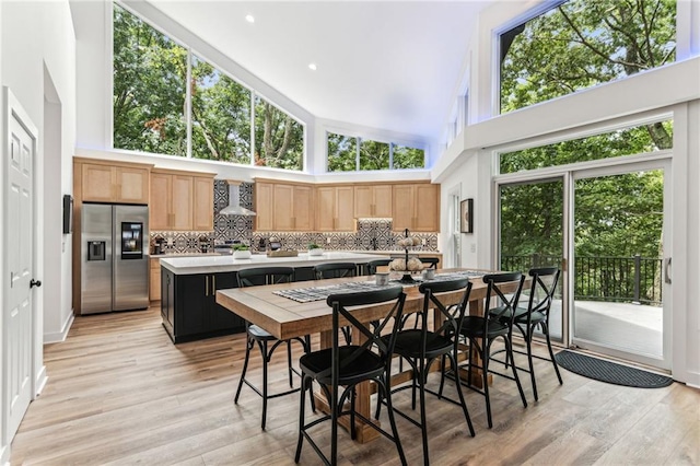 kitchen with a kitchen island, light countertops, backsplash, stainless steel fridge with ice dispenser, and wall chimney exhaust hood