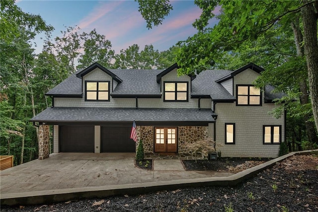 exterior space featuring stone siding, concrete driveway, roof with shingles, and french doors