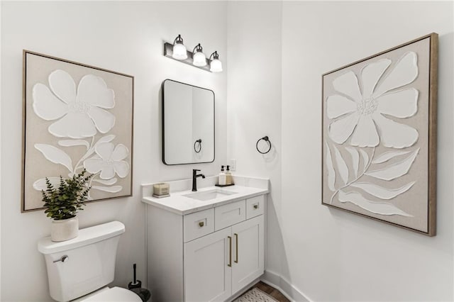 half bathroom featuring toilet, vanity, and baseboards