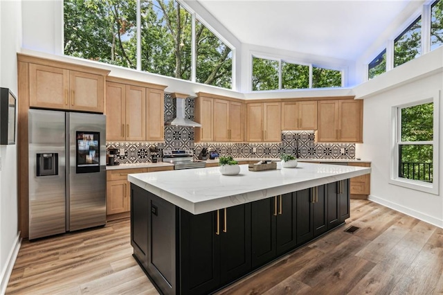 kitchen with a center island, appliances with stainless steel finishes, wall chimney range hood, dark cabinetry, and decorative backsplash