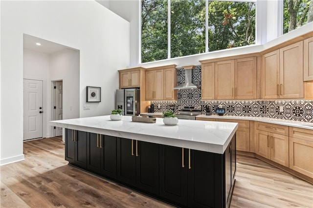 kitchen with a towering ceiling, appliances with stainless steel finishes, a kitchen island, wall chimney range hood, and dark cabinets