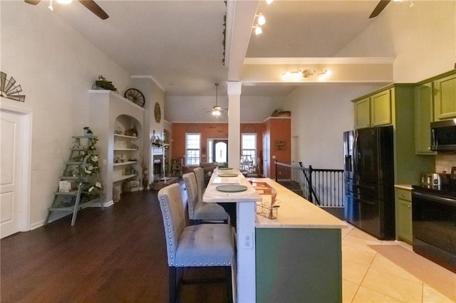 kitchen featuring ceiling fan, green cabinetry, light countertops, a kitchen breakfast bar, and black appliances