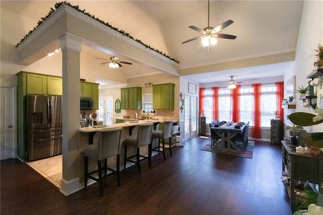 kitchen with hardwood / wood-style floors, kitchen peninsula, appliances with stainless steel finishes, green cabinets, and a breakfast bar area