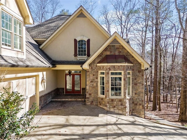 property entrance with stucco siding, a shingled roof, stone siding, and french doors