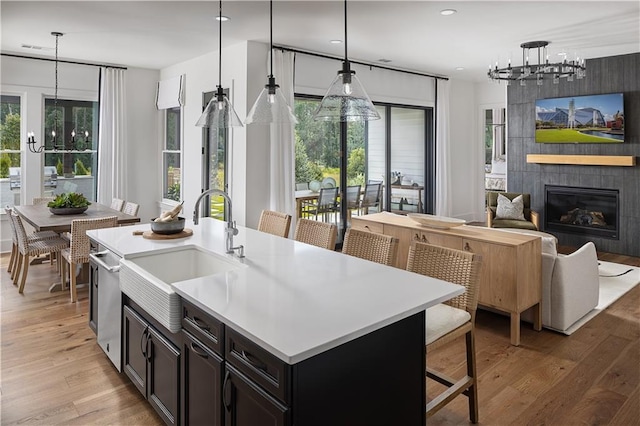 kitchen with decorative light fixtures, a tile fireplace, sink, a healthy amount of sunlight, and an island with sink