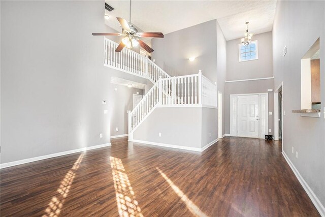 entrance foyer featuring ceiling fan with notable chandelier, a towering ceiling, and dark wood-type flooring