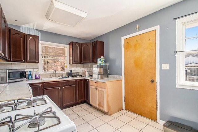 kitchen with gas range gas stove, a sink, light countertops, backsplash, and stainless steel microwave