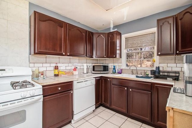 kitchen with light tile patterned floors, white appliances, a sink, light countertops, and tasteful backsplash