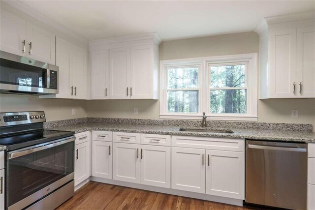 kitchen with light stone counters, sink, wood-type flooring, white cabinetry, and stainless steel appliances