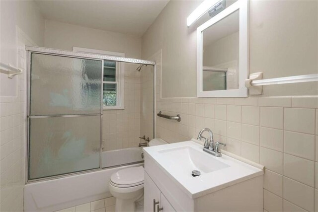 full bathroom featuring vanity, bath / shower combo with glass door, tile walls, tile patterned flooring, and toilet