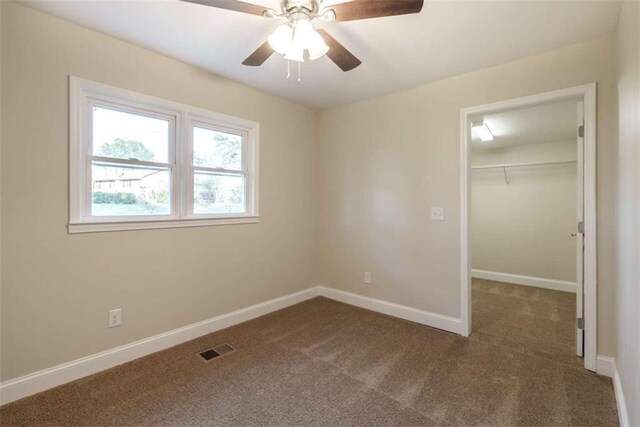 unfurnished bedroom featuring a spacious closet, ceiling fan, a closet, and dark carpet