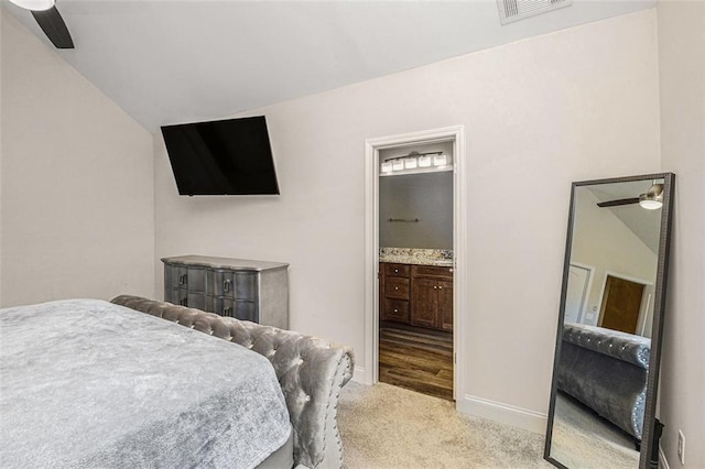 bedroom with light colored carpet, visible vents, vaulted ceiling, connected bathroom, and baseboards