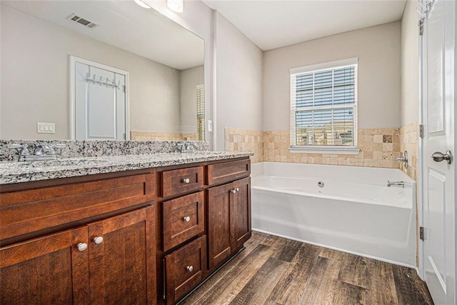 full bathroom with double vanity, visible vents, wood finished floors, a garden tub, and a sink