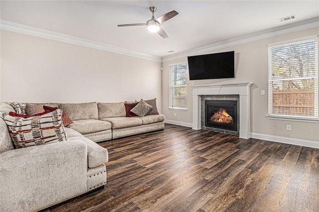 living area with a tiled fireplace, visible vents, dark wood finished floors, and crown molding