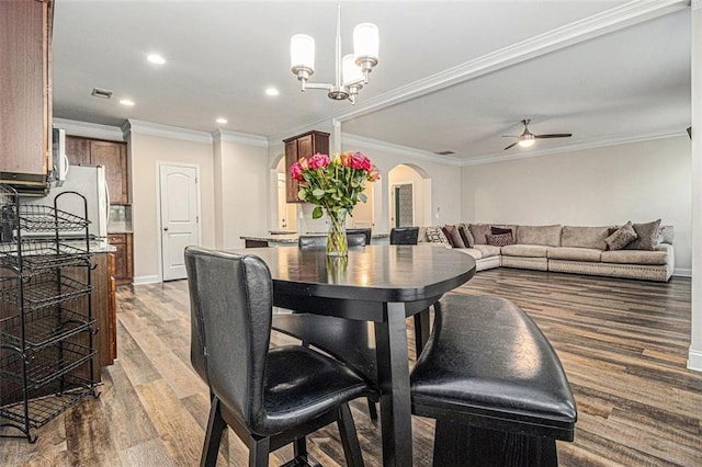 dining space featuring arched walkways, ceiling fan with notable chandelier, wood finished floors, visible vents, and ornamental molding