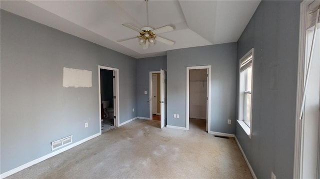 unfurnished bedroom featuring ceiling fan, ensuite bathroom, a spacious closet, light colored carpet, and a closet