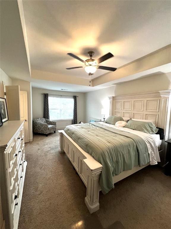 bedroom with ceiling fan, a raised ceiling, and dark carpet