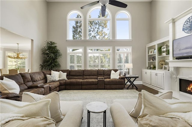 living area with a warm lit fireplace, plenty of natural light, dark wood-style floors, and ceiling fan with notable chandelier