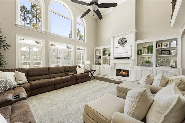 living room featuring a lit fireplace, wood finished floors, a ceiling fan, and crown molding