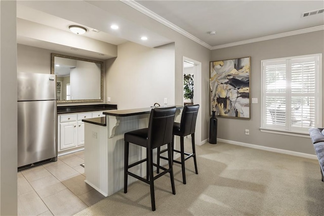 kitchen with crown molding, a breakfast bar area, visible vents, freestanding refrigerator, and a peninsula