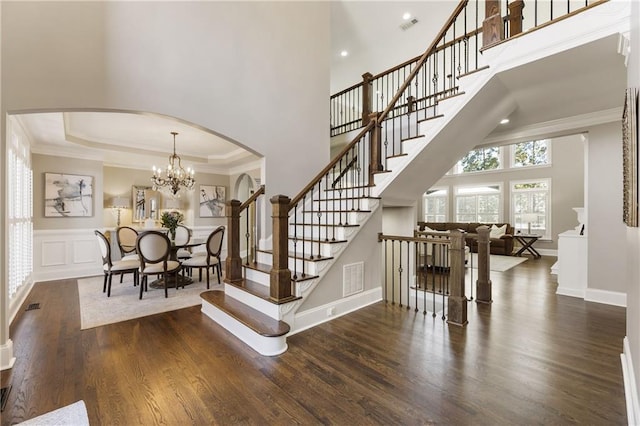 foyer featuring a chandelier, arched walkways, wood finished floors, visible vents, and ornamental molding